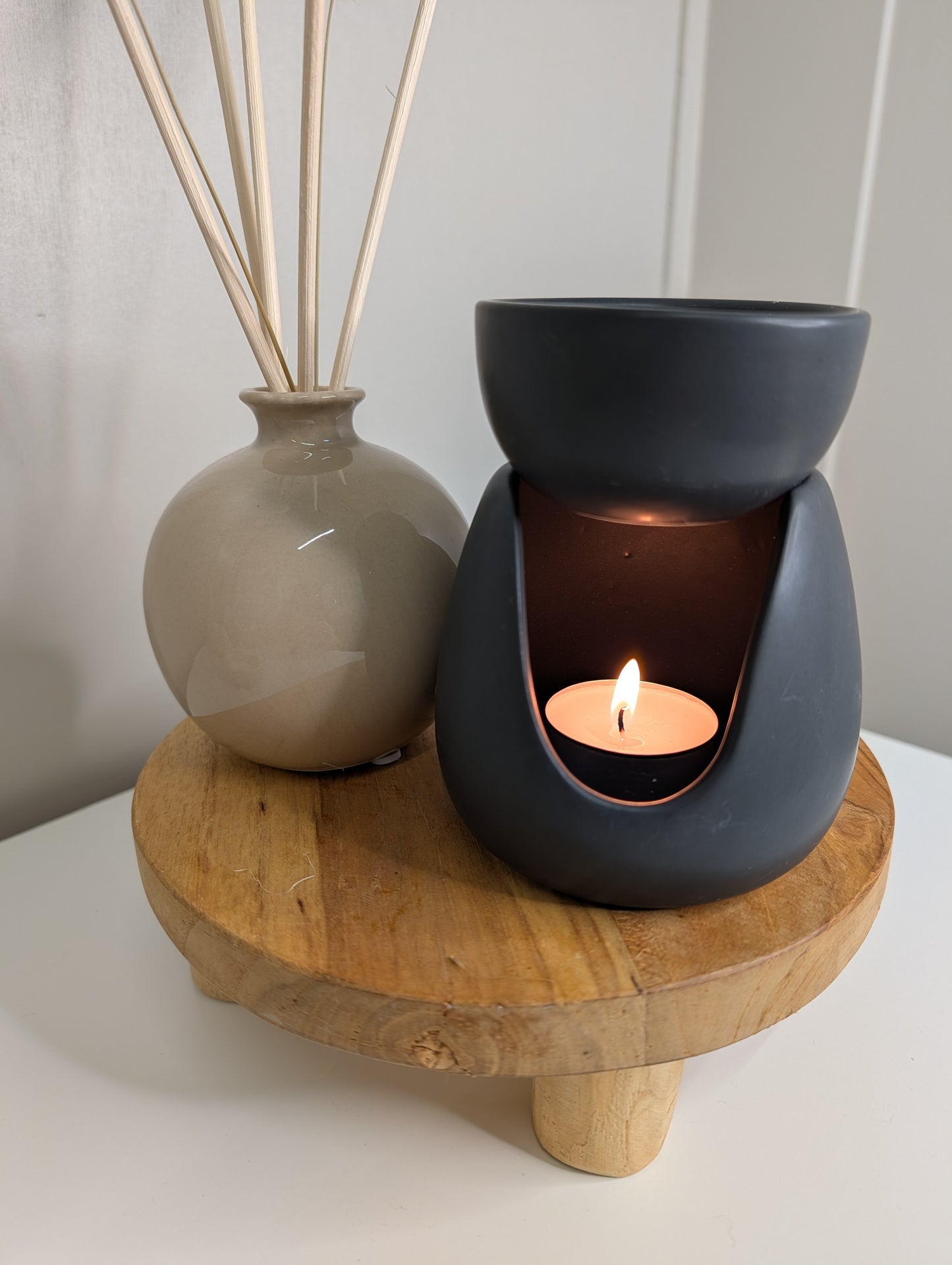 Ceramic Stoneware Wax Warmer on a wooden stand with a tealight candle and decorative vase in the background.