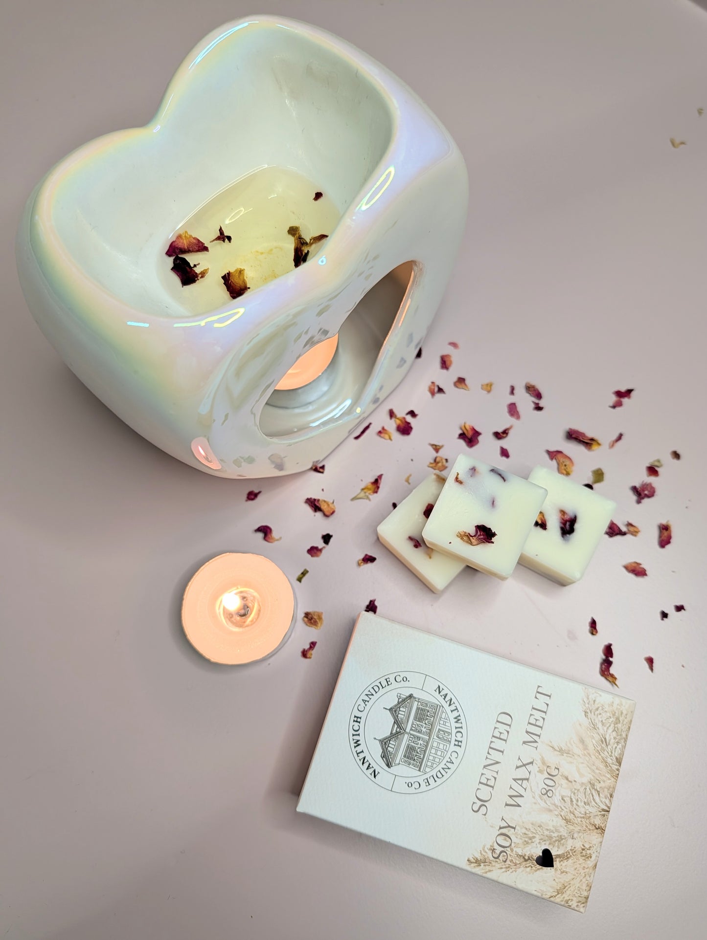 Rhubarb & Rose Scented Soy Wax Melt Box alongside a wax melt warmer, candle, and dried rose petals.