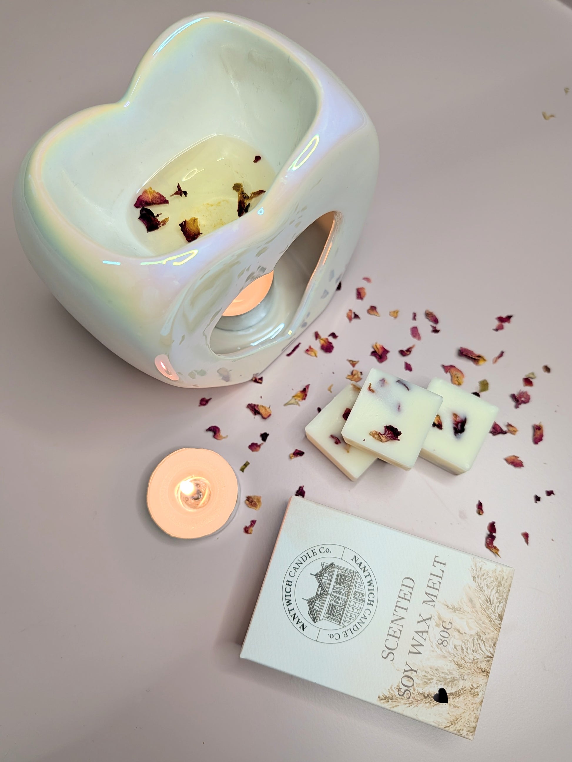 Rhubarb & Rose Scented Soy Wax Melt Box alongside a wax melt warmer, candle, and dried rose petals.